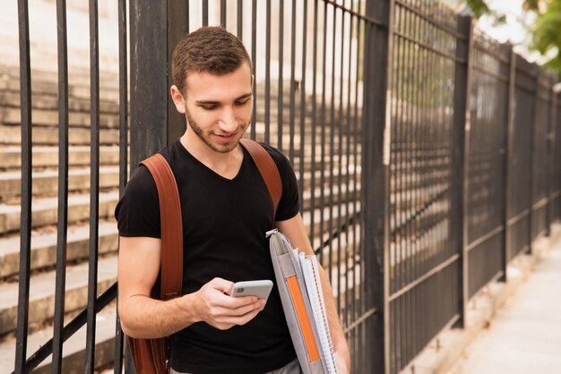 Obsługuje patrzeć jego telefon obok wysokiego ogrodzenia