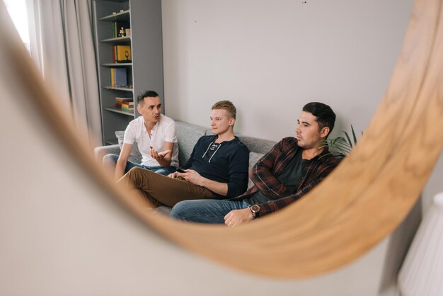 Odbicie w lustrze trzech przyjaciół firmy. młodzi faceci siedzą na miękkiej kanapie w domu i bawią się rozmową