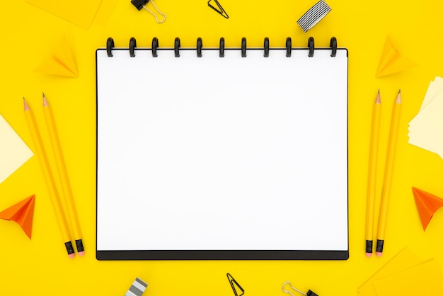 Bezpłatne zdjęcie odgórnego widoku materiały układ na żółtym tle z pustym notatnikiem