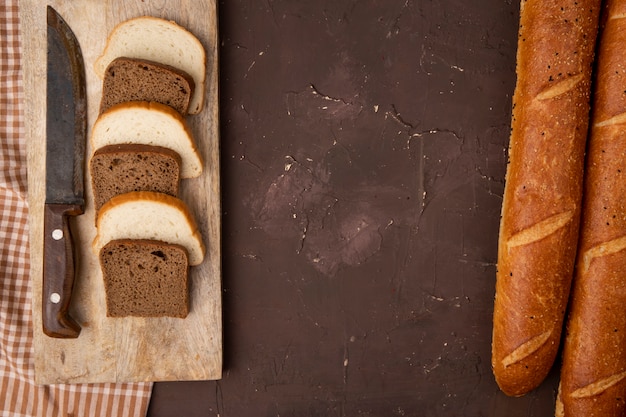 Odgórny widok białego i czarnego chleba plasterki i nóż na tnącej desce z baguettes na wałkoniącego się tle z kopii przestrzenią