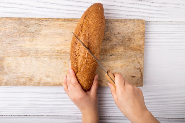 Odgórny widok kobieta wręcza tnącego baguette z nożem na tnącej desce na drewnianym tle