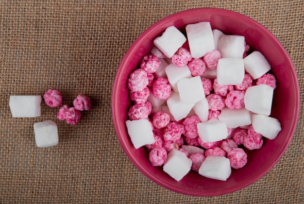 Odgórny widok kolorowi cukrowi cukierki z cukrowymi sześcianami w pucharze na parcianym tekstury tle