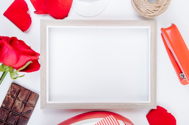 Bezpłatne zdjęcie odgórny widok pusta obrazek rama z piłką linowa czerwonego koloru róża, ciemna czekolada i zszywacz na białym tle z kopii przestrzenią