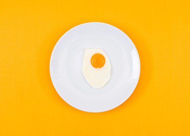 Odgórny widok smażący jajko na bielu talerzu i na kolor żółty powierzchni horyzontalnym