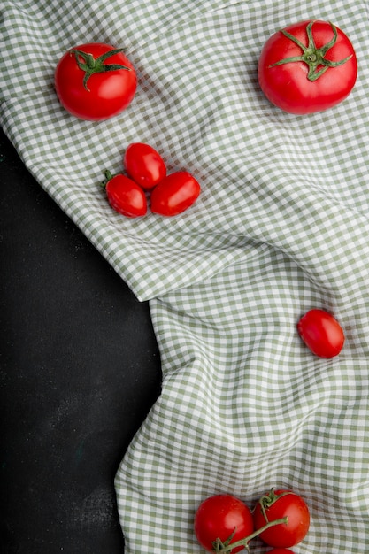 Odgórny widok świezi dojrzali czerwoni pomidory na szkockiej kraty tablecloth na czarnym tle