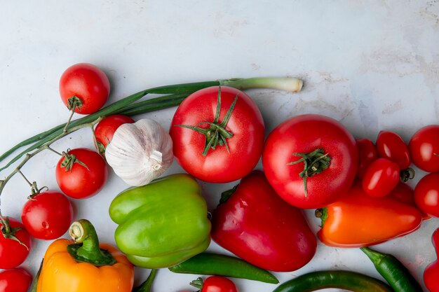 Odgórny widok świezi dojrzali warzywa jako pomidorów kolorowi dzwonkowi pieprze zielonego chili pieprzu czosnek i zielone cebule na białym tle