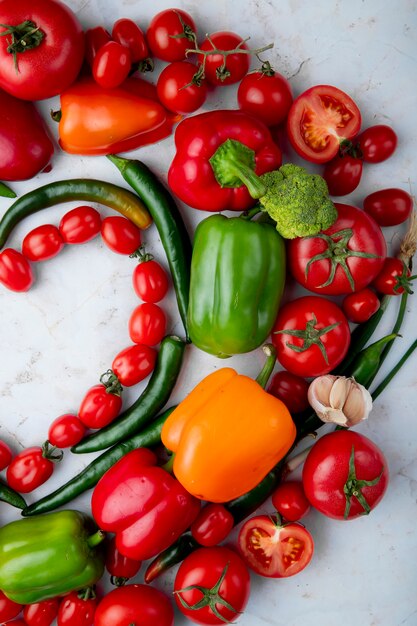 Odgórny widok świezi dojrzali warzywa układający w kierowym kształcie czereśniowych pomidorów zielonego chili pieprzu dzwonkowego pieprzu czosnek i cebula na marmurowym tle