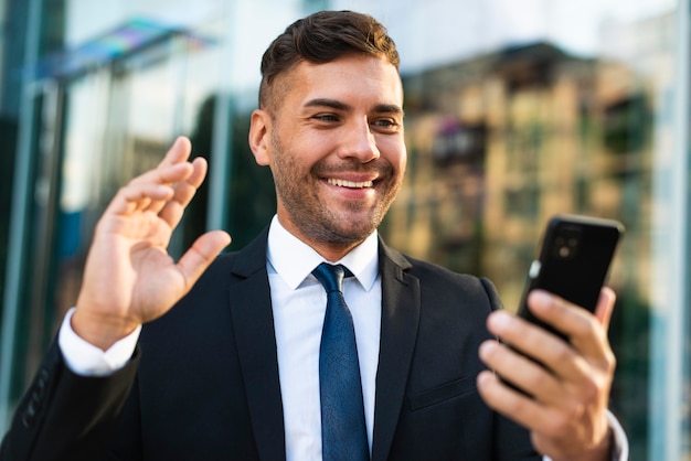 Bezpłatne zdjęcie odkryty biznesmen trzymając telefon i uśmiecha się