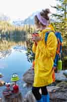 Bezpłatne zdjęcie odkryty pionowe ujęcie zamyślonej kobiety hicker trzyma gorący napój w filiżance, sprawia, że napój na specjalnym sprzęcie turystycznym