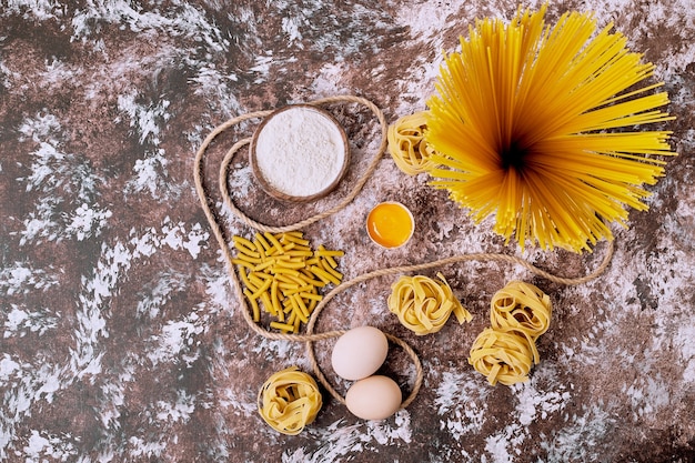 Bezpłatne zdjęcie odmiana surowych makaronów z jajkiem i mąką na drewnianym stole.