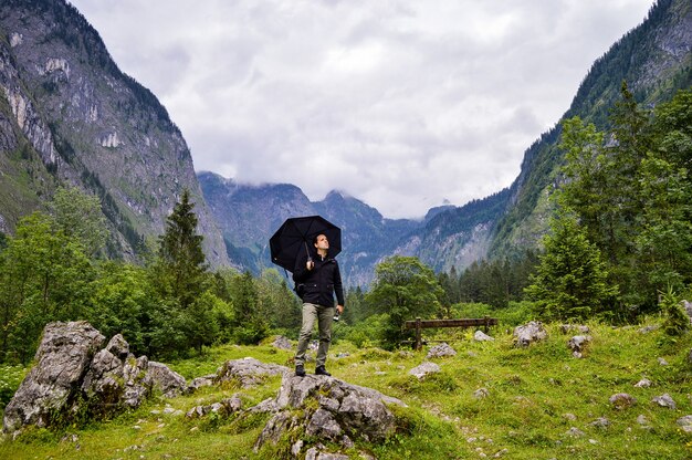 Odważny turysta stojący na skale z parasolem i patrząc na piękne góry