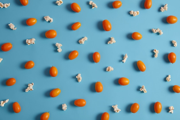 Odżywcze pomarańczowe nieobrane owoce cumquat zawierające witaminy i popcorn na białym tle na niebieskim tle. Dojrzałe, zdrowe owoce do odżywiania. Koncepcja surowej diety. Selektywna ostrość. Odmiana Nagami