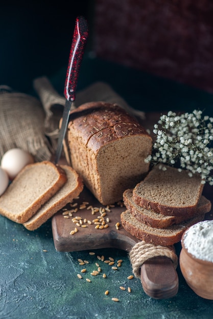 Bezpłatne zdjęcie ogólny widok dietetycznego czarnego chleba pszenicy na drewnianej desce do krojenia nóż kwiat jaja mąka w misce brązowy ręcznik na tle mieszanych kolorów