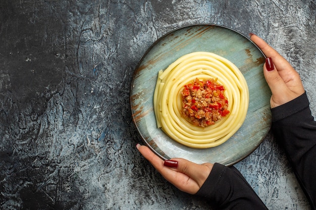 Ogólny widok dłoni trzymającej pyszny makaron na niebieskim talerzu podawany z pomidorem i mięsem na obiad po lewej stronie na lodowym tle