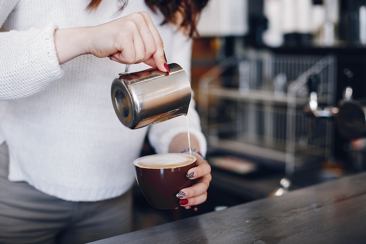 Bezpłatny plik Zdjęcie ogólny widok kobiet barista wlewając piankę mleka do cappuchino w kawiarni