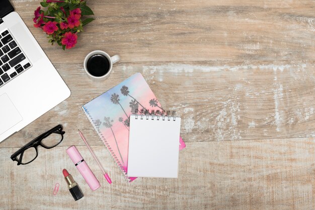 Ogólny widok laptopa; szminka; Zakreślacz; notes spiralny; filiżanka kawy; długopis; i okulary na drewnianym stole biurowym