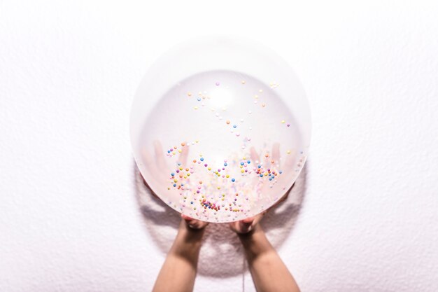 Ogólny widok ręki osoby trzymającej biały balon z kolorową posypką na białym tle z teksturą