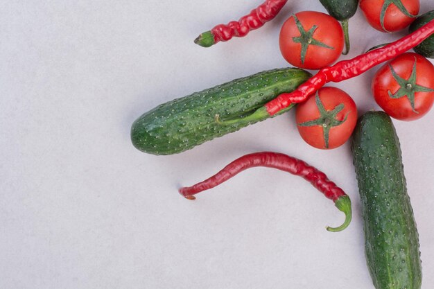 Ogórki, papryczki chili i pomidory na białym stole.