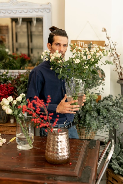 Ogrodnik trzyma duży wazon z liśćmi i kwiatami