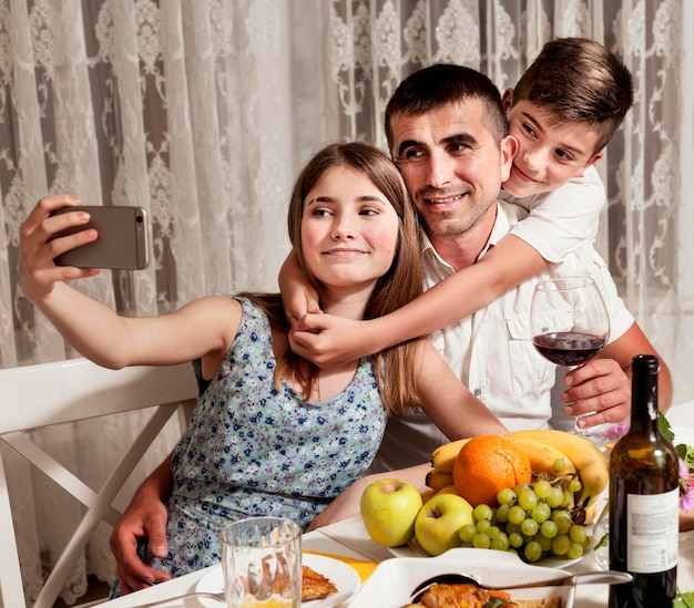 Bezpłatne zdjęcie ojciec biorąc selfie z dziećmi przy stole