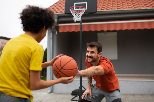 Bezpłatne zdjęcie ojciec i syn grają razem w koszykówkę na podwórku