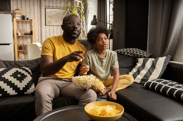 Ojciec i syn jedzą razem popcorn i chipsy ziemniaczane na kanapie