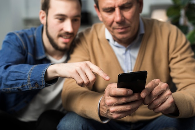 Bezpłatne zdjęcie ojciec i syn patrzeje telefon w żywym pokoju