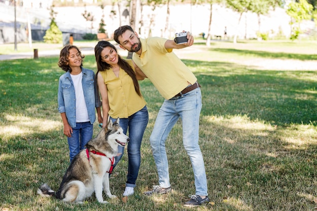 Ojciec robi selfie żony i dziecka w parku z psem