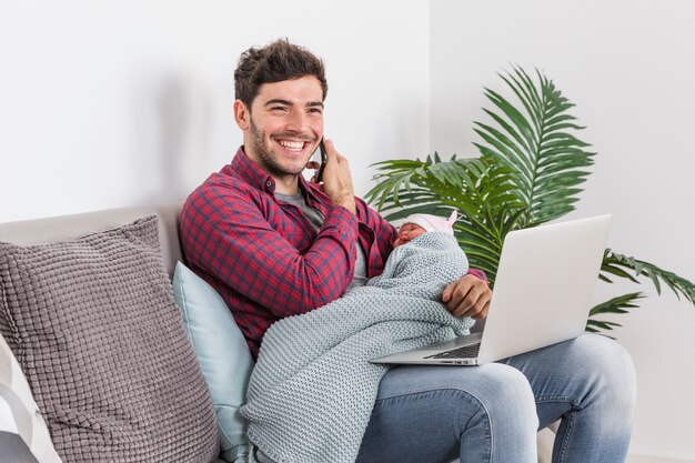 Ojciec z dzieckiem rozmawia przez telefon i za pomocą laptopa