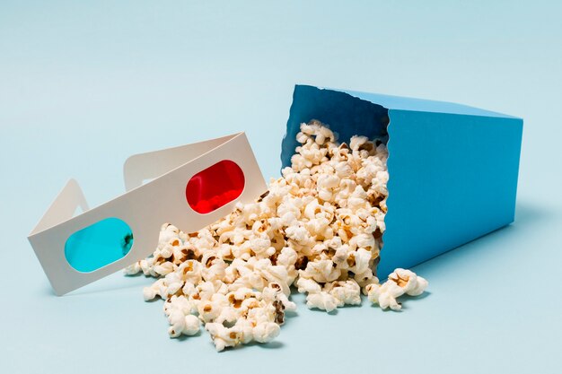 Okulary 3D w pobliżu rozlanego popcornu z pudełka na niebieskim tle