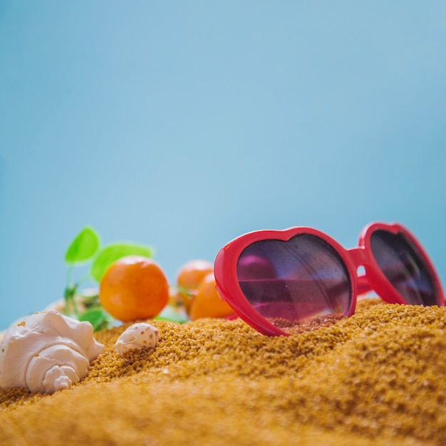 Bezpłatne zdjęcie okulary przeciwsłoneczne i pomarańcze na piasku