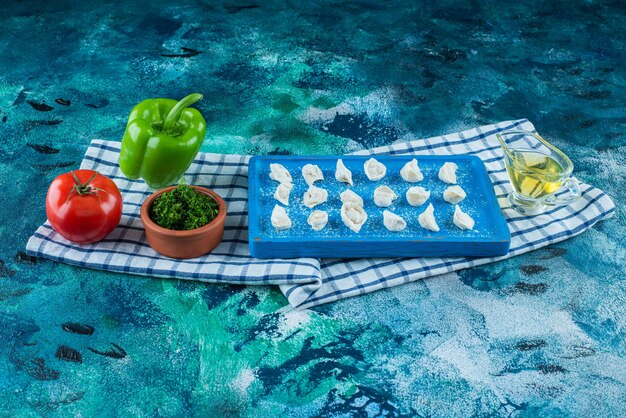 Olej i warzywa obok tureckich ravioli na desce na ściereczce, na niebieskim stole.