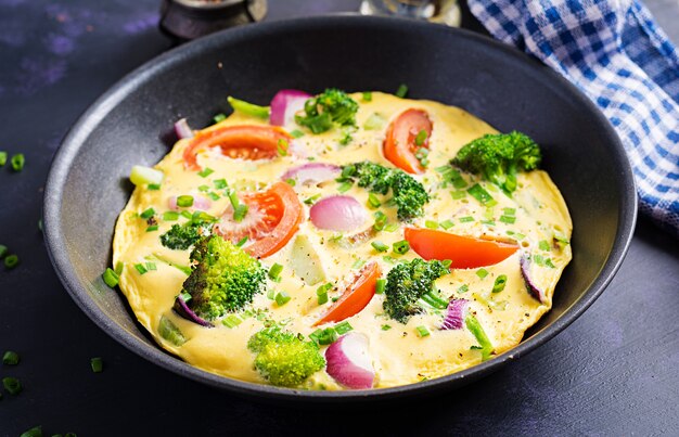 Omlet z brokułami, pomidorami i czerwoną cebulą na żelaznej patelni. Włoska frittata z warzywami.