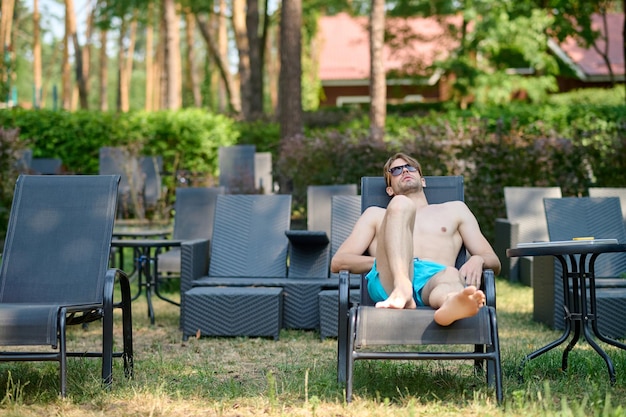 Opalanie się. Młody mężczyzna w niebieskich spodenkach opala się i wygląda na zrelaksowanego