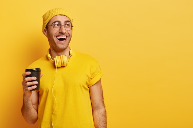 Optymistyczny mężczyzna w okularach śmieje się, spędzając czas z przyjaciółmi podczas przerwy na kawę, trzyma jednorazowy kubek, odwraca wzrok