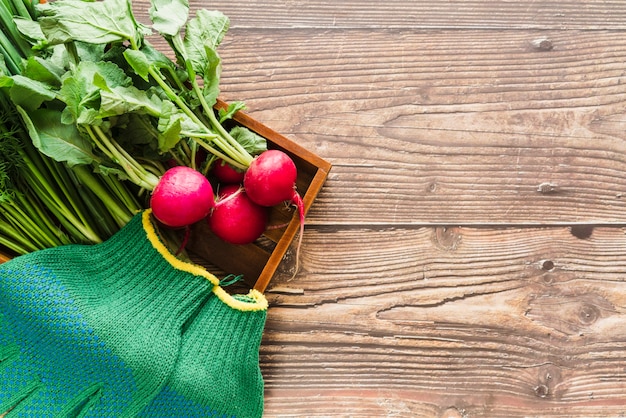 Organiczna rzepa i zielone rękawiczki ogrodnicze w drewnianej tacy nad drewnianym biurkiem