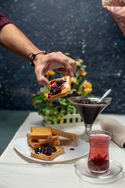 Osoba biorąca toast z dżemem. Wokół szklanka czarnej herbaty.