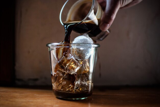 Osoba nalewa gorącą kawę do szklanki z lodem