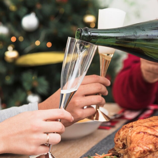 Osoba nalewa szampana w szkle przy boże narodzenie stołem
