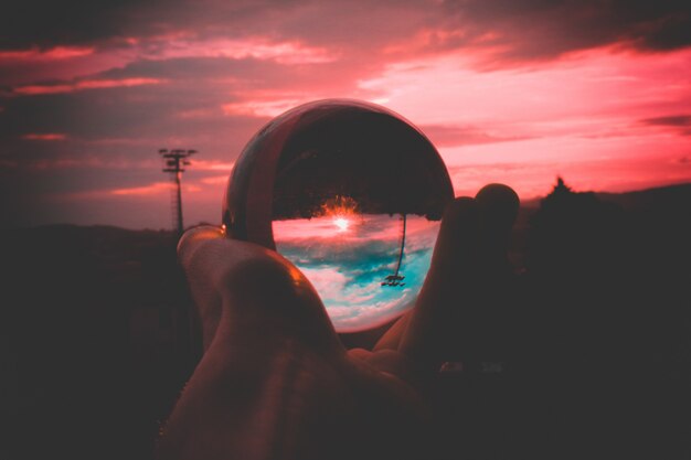 Osoba trzymająca szklaną kulę z odbiciem kolorowego nieba i pięknego zachodu słońca