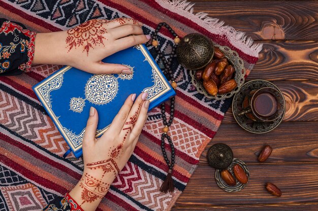 Osoba z mehndi trzymając książkę Koran w pobliżu filiżanki herbaty