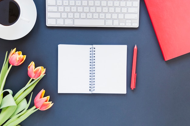 Otwarty notatnik w pobliżu filiżanki kawy i klawiatury na biurku z kwiatami tulipanów