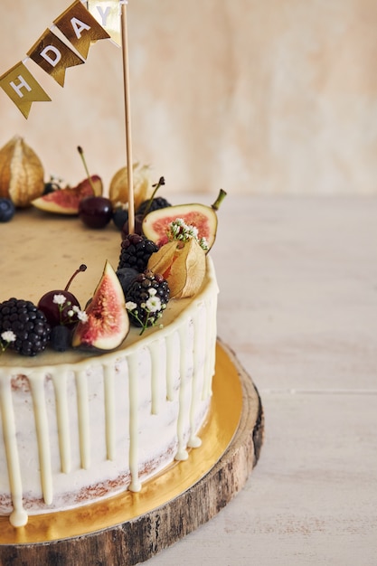 Owocowy tort urodzinowy z topperem, owocami na wierzchu i białą kroplą na beżowym kolorze