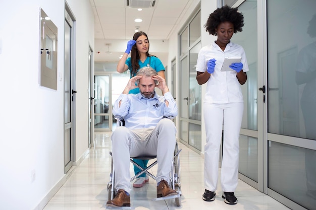 Bezpłatne zdjęcie pacjent na wózku inwalidzkim z profesjonalnym, afroamerykańskim lekarzem specjalistą i pielęgniarką na korytarzu szpitalnego centrum rekonwalescencji