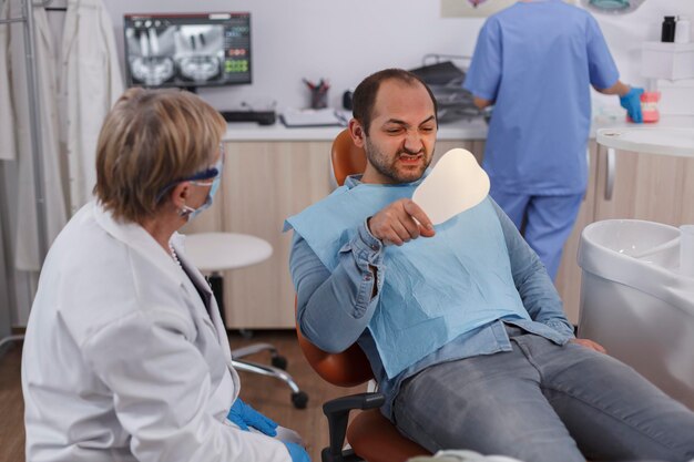 Pacjent trzyma lusterko patrząc na zabieg zębów po zabiegu stomatologicznym podczas badania stomatologicznego w gabinecie stomatologicznym. Dentysta starsza kobieta wyjaśniająca higienę jamy ustnej. Pojęcie medycyny