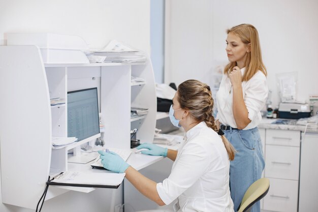 Pacjentka kobieta w gabinecie lekarskim. Lekarz w masce medycznej. Lekarz korzysta z komputera.