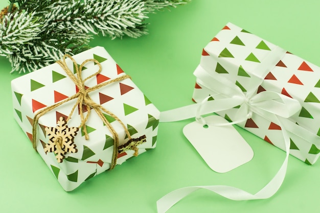 Pakowane prezenty w świąteczny papier na zielonym tle z gałązką świerka na śniegu. ozdobiony płatkami śniegu. karta za gratulacje.