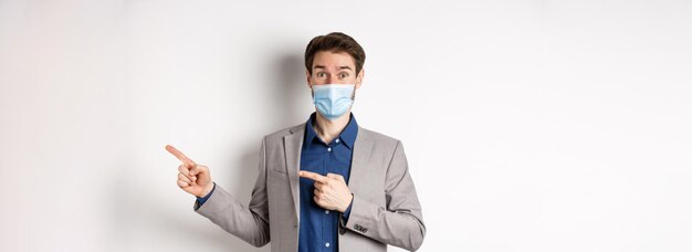 Pandemia Covid i koncepcja biznesowa podekscytowany męski przedsiębiorca w masce medycznej i garniturze wskazującym palcem
