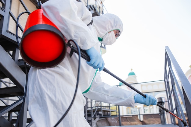 Bezpłatne zdjęcie pandemia wirusa koronawirusa. środek dezynfekujący w kombinezonie ochronnym i masce rozpyla środki dezynfekujące w pomieszczeniu.