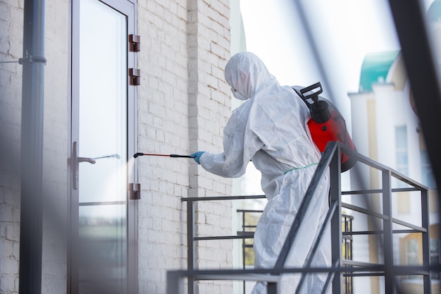 Pandemia wirusa koronawirusa. Środek dezynfekujący w kombinezonie ochronnym i masce rozpyla środki dezynfekujące w pomieszczeniu.